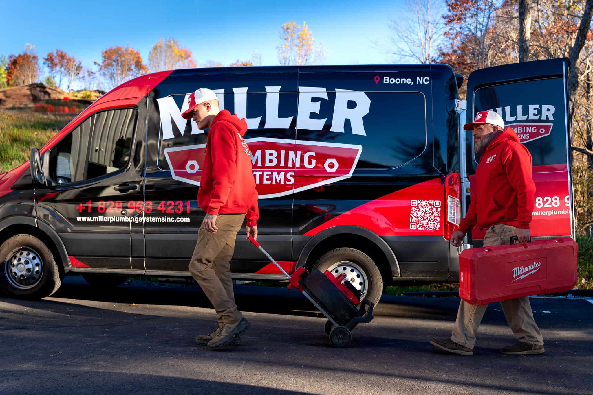 Two Miller Plumbing techs walking gear out to the van