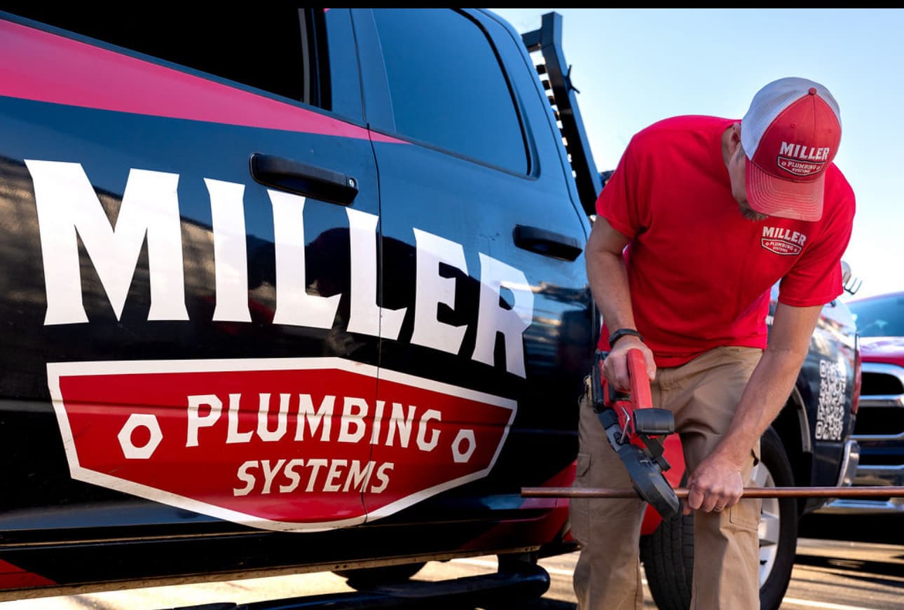 A Miller Plumbing technician at the side of a service truck, working on a copper line.